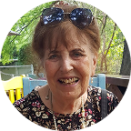 Tonia Cope Bowley, a woman with short brown hair, wearing sunglasses on her head and a floral top, smiling outdoors.